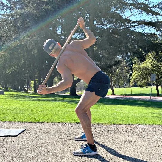 Athlete practices bentover torso rotations with pole, to improve spinal mobility.