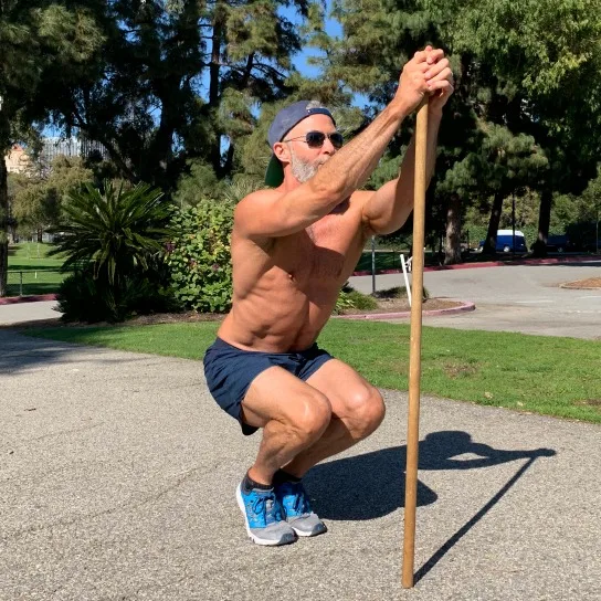 Male athlete uses pole to assist in doing narrow squats for ankle flexibility.