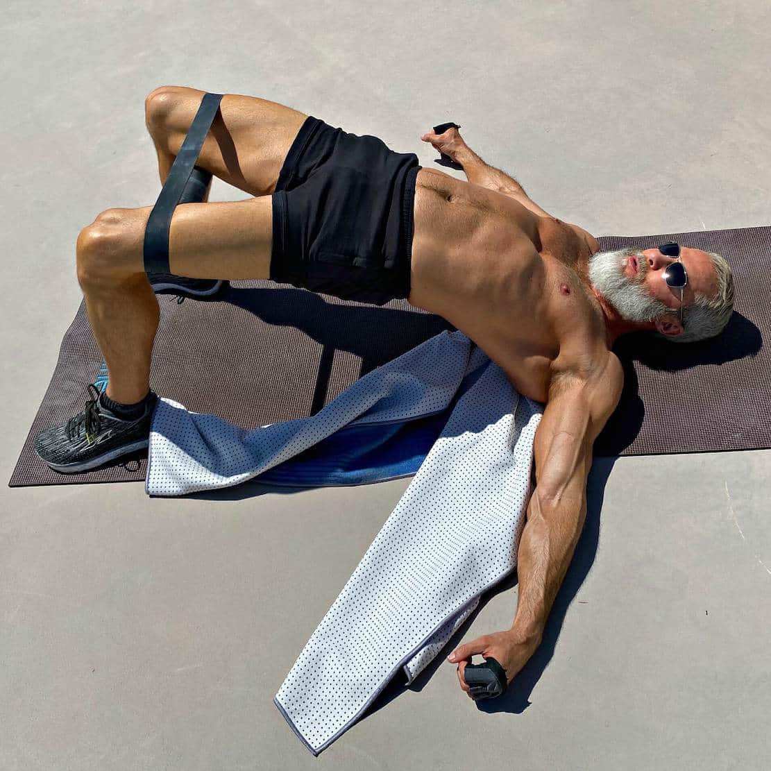 Silver-bearded man does glute bridge exercise with resistance bands.