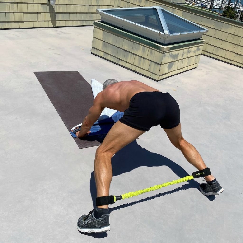 Man exercising outdoors on rooftop using resistance band on legs.