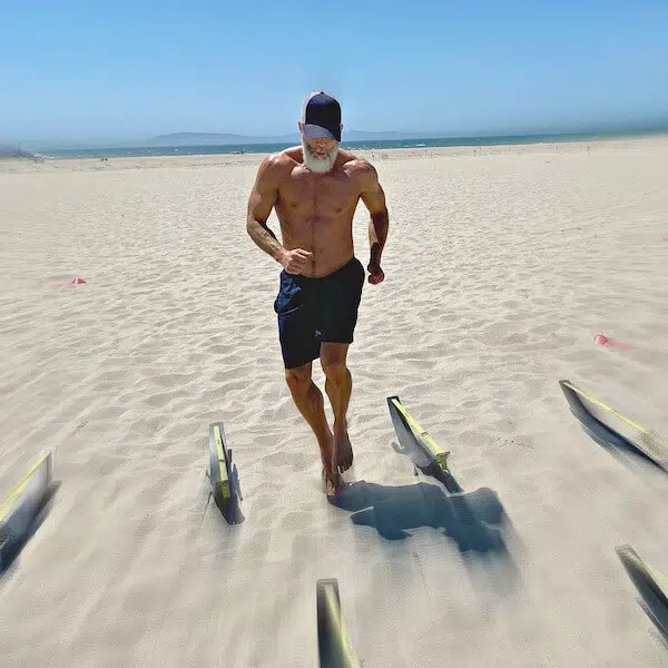 Silver-bearded athlete does workout at the beach barefoot in the sand.
