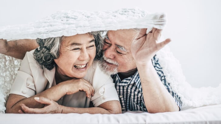 mature couple hiding under covers laughing enjoying good mental health and wellness